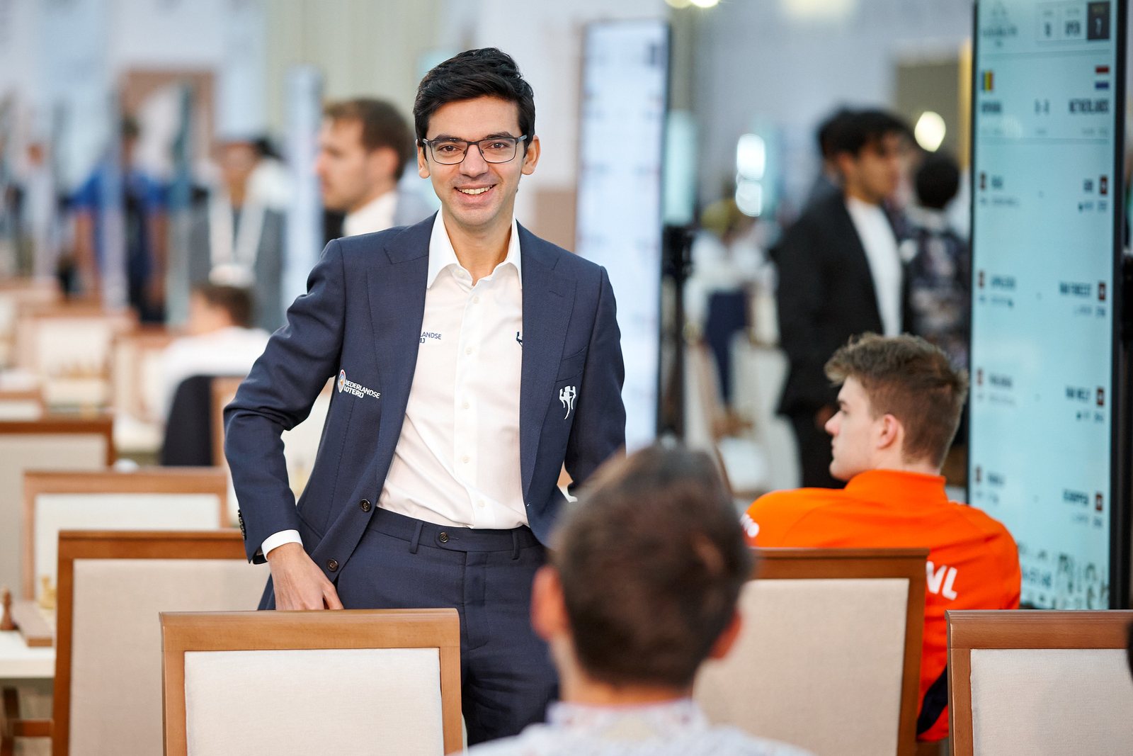 Anish Giri lângă masa de joc, cu ecranul meciului România-Olanda în dreapta