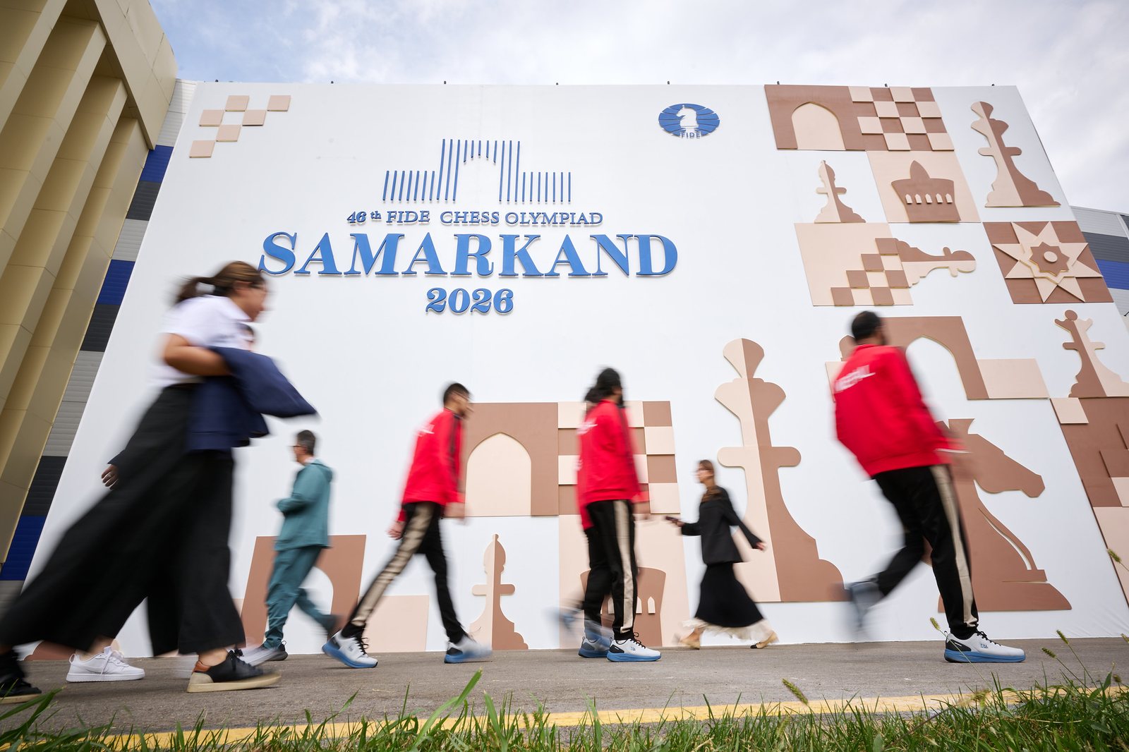 Oameni trecând prin fața panoului Samarkand 2026 al Olimpiadei